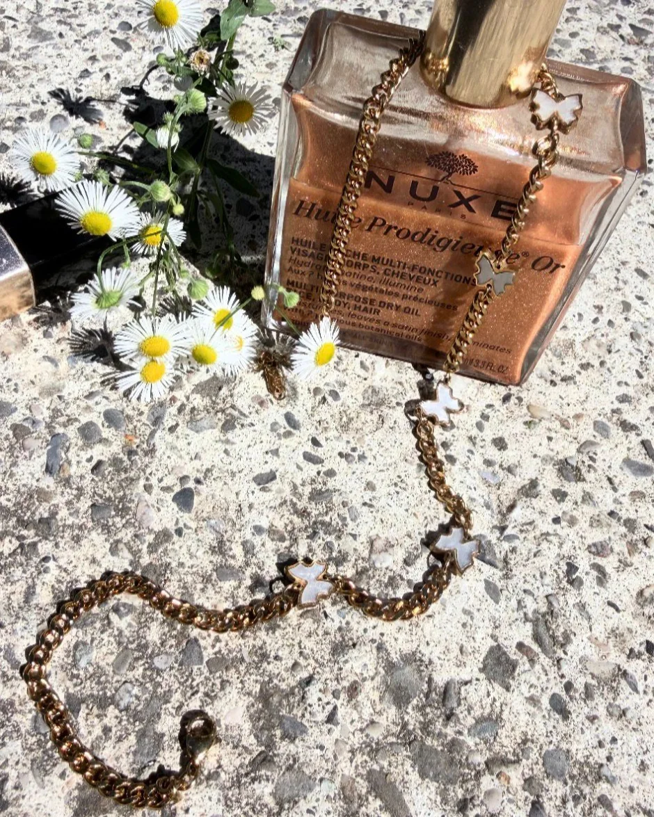 Collier Céleste ton or serpentant sur un béton clair, marguerites sauvages