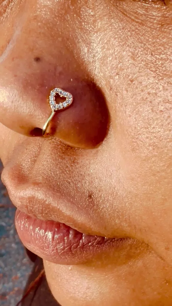 Le faux piercing Lovely en cœur pavé, porté à l'aile du nez, en gros plan au soleil